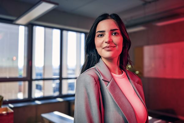 Frau steht in einem Bürogebäude und lächelt seitlich in die Kamera
