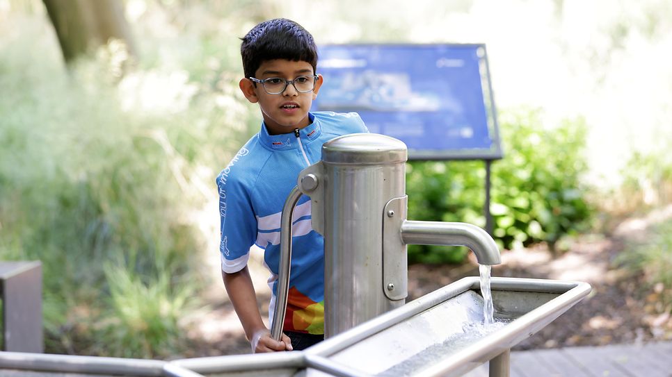 Junge spielt an einer Wasserpumpe in einem Park