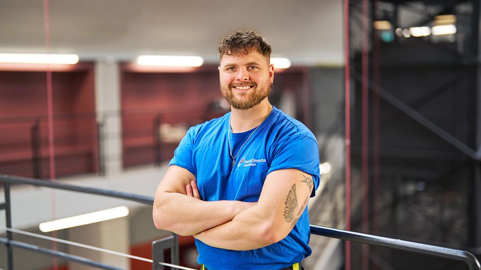 Marcel Mück steht in Arbeitskleidung in einer Halle.