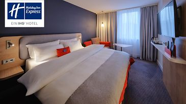 Modernes Hotelzimmer mit großem Doppelbett, Sitzbereich, Fernseher und bodentiefen Vorhängen.