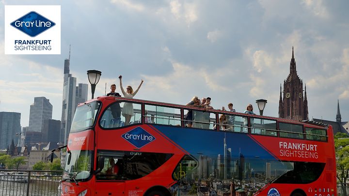 Roter Doppeldeckerbus für Stadtrundfahrten fährt durch Frankfurt, mit Skyline und Dom im Hintergrund.