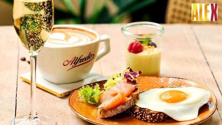 Frühstück mit Spiegelei, Lachs, Dessert, Kaffee und Sekt auf einem gedeckten Tisch serviert.