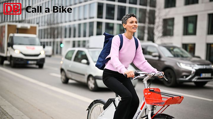 Person fährt mit einem Leihfahrrad durch die Stadt, im Hintergrund sind Autos und moderne Gebäude zu sehen.