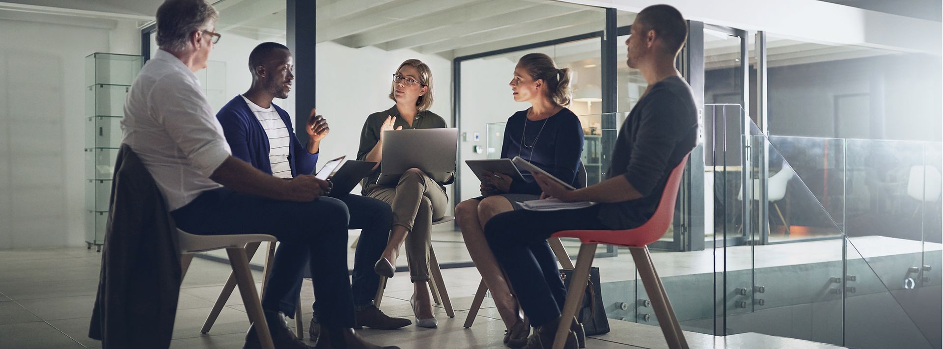Fünf Personen mit Laptops sitzen in einem Stuhlkreis und unterhalten sich
