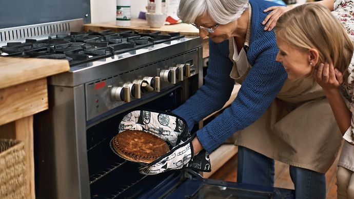 © iStock.com/PeopleImages Mutter holt Kuchen aus dem Gasbackofen