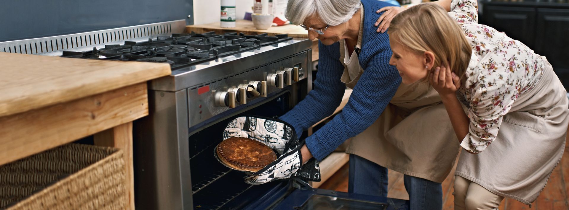 © iStock.com/PeopleImages Mutter holt Kuchen aus dem Gasbackofen