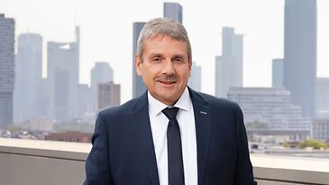 Mann im Anzug mit Krawatte steht auf einer Terrasse vor einer Skyline. Professioneller, formeller Ausdruck.