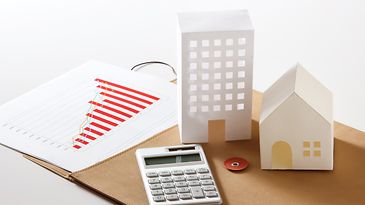 © stock.adobe.com/taa22 Modellhäuser aus Papier und ein Taschenrechner