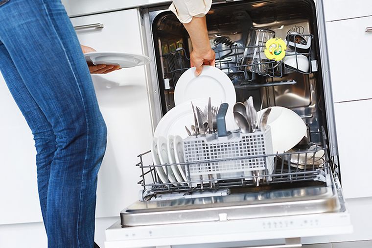 Frau räumt Geschirr in Geschirrspüler