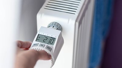 © stock.adobe.com/Daniel Jędzura Hand programmiert ein Thermostatventil an einer Heizung