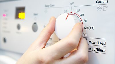 © iStock.com/Daisy-Daisy Hand stellt Temperatur an der Waschmaschine auf 30 Grad ein