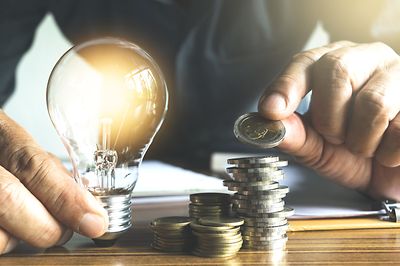 © stock.adobe.com/mintra Mann hält Glühbirne und zählt Münzgeld