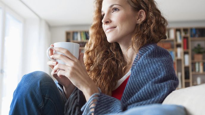 © Junge Frau im Seitenprofil sitzt auf der Couch und hält Tasse in beiden Händen Mainova Wärme Classic – Fernwärme für Frankfurt