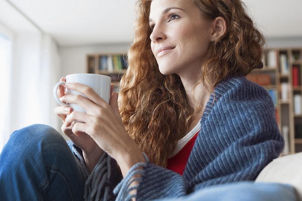 © Junge Frau im Seitenprofil sitzt auf der Couch und hält Tasse in beiden Händen Mainova Wärme Classic – Fernwärme für Frankfurt