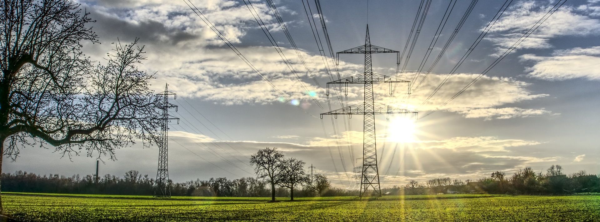 Freileitungsmasten auf einem Feld, Sonne strahlt am Himmel