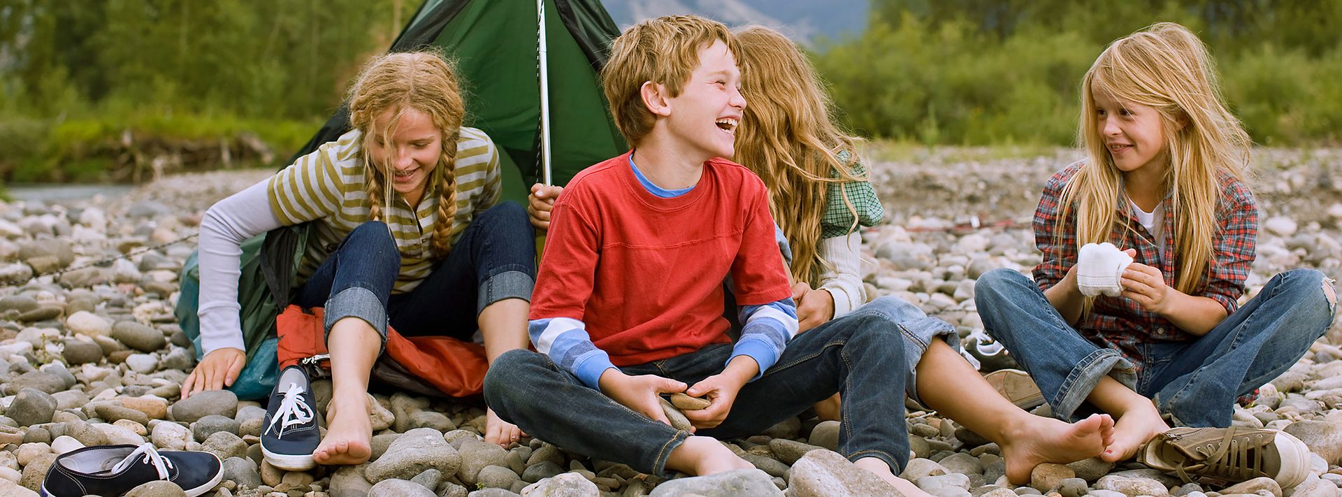 Vier fröhliche Kinder sitzen vor einem Zelt am Steinstrand