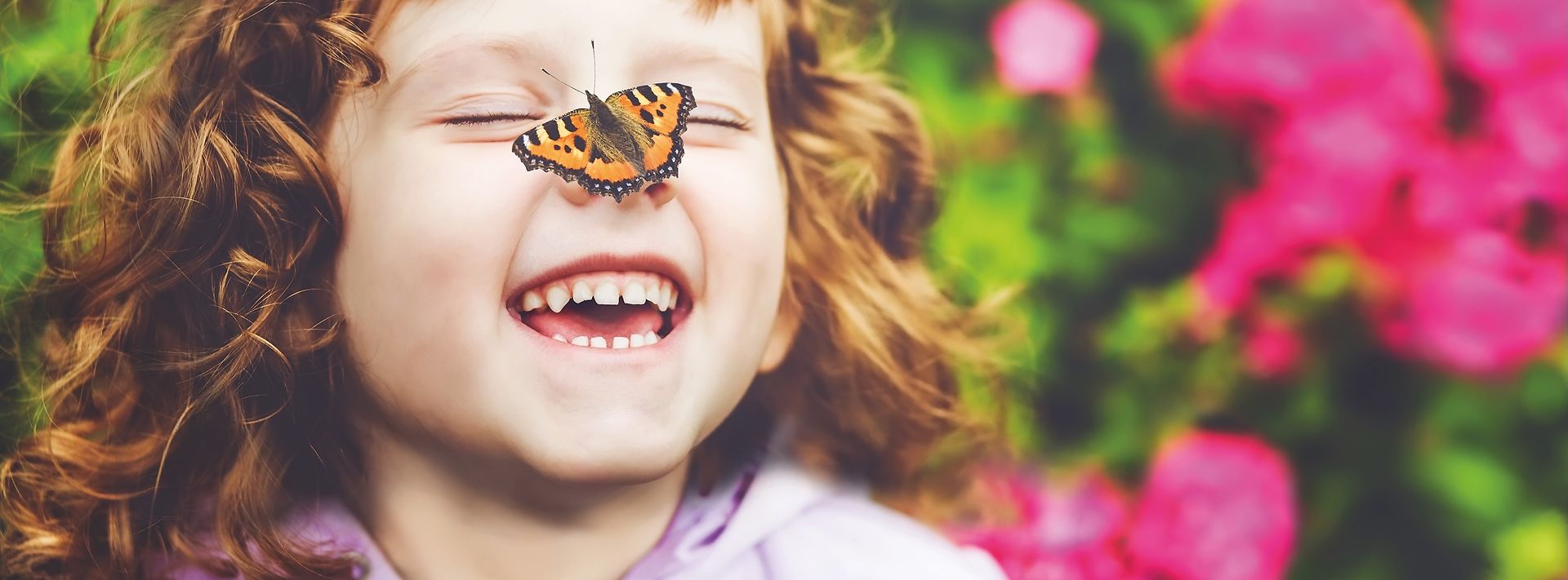 Schwarz-orange gemusterter Schmetterling landet auf der Nase eines kleinen Mädchens, welches lacht.