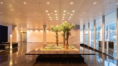 © Mainova Modernes Foyer mit glänzendem Boden, heller Deckenbeleuchtung und einem zentralen Pflanzenarrangement.