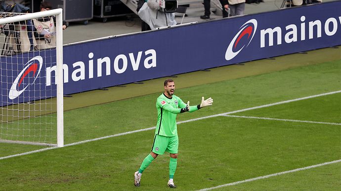 Ein Torwart in grüner Uniform steht auf einem Fußballfeld vor dem Tor.