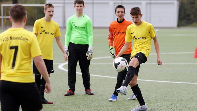 Vier Fußballspieler in gelben Trikots und ein Torwart in grünem Trikot spielen auf einem Kunstrasenplatz.