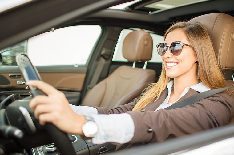 Lächelnde Frau mit Sonnenbrille sitzt am Lenkrad eines Autos.