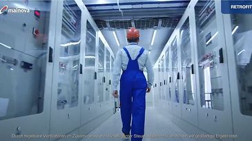 © Mainova Ein Arbeiter mit rotem Helm und blauer Kleidung geht durch einen Gang mit grauen Schaltschränken