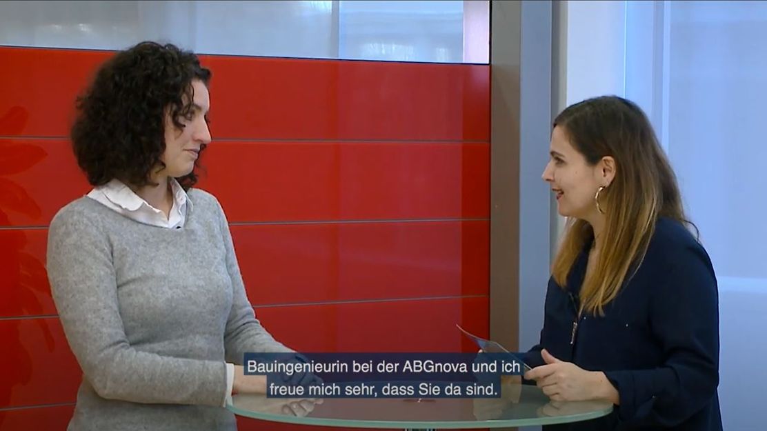 © Mainova Zwei Frauen stehen an einem Tisch und sprechen miteinander. Eine trägt ein Namensschild.