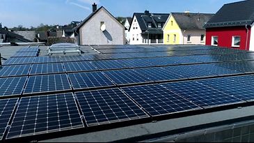 Auf einem Dach sind mehrere Reihen von Solarpaneelen installiert, im Hintergrund sind bunte Häuser zu sehen.
