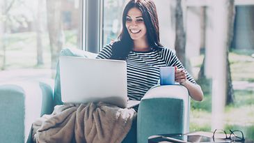 Frau sitzt mit Laptop und Kaffeetasse auf türkisem Sessel