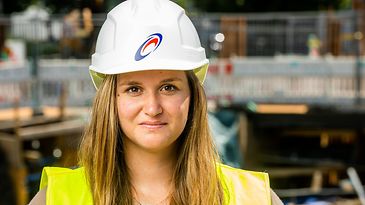 Eine Person mit Schutzhelm und Warnweste auf einer Baustelle.
