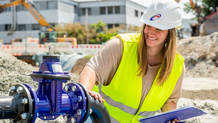 Frau mit Helm und Warnweste prüft eine Pumpe auf einer Baustelle