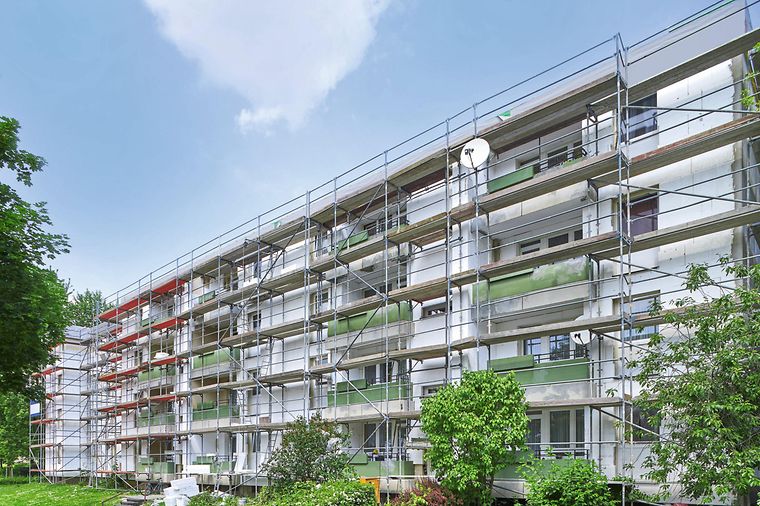 Ein mehrstöckiges Gebäude mit Gerüsten an der Fassade, umgeben von Bäumen und Grünflächen.