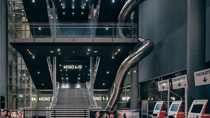 Ein modernes Kinofoyer mit Treppen, Rollrutsche, Ticketautomaten und Beschilderung für Kinosäle 1-10.