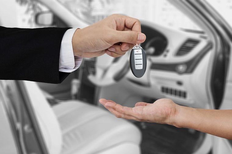 Eine Hand übergibt einen Autoschlüssel an eine andere Hand vor dem Hintergrund eines Autoinnenraums.