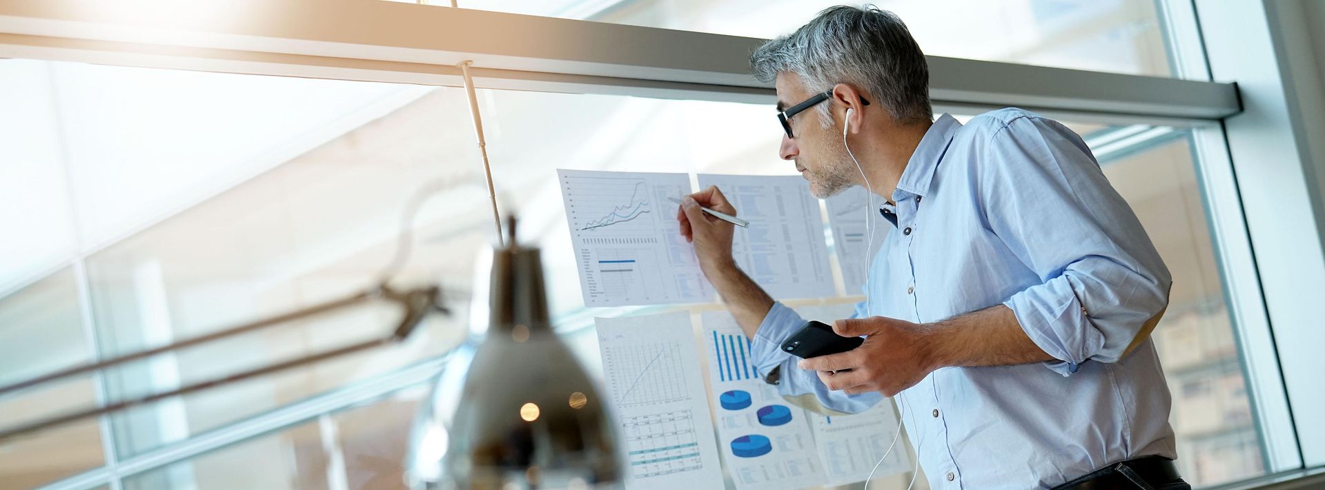 © stock.adobe.com/goodluz Geschäftsmann macht Notizen auf Diagrammen, die an einer Glasscheibe hängen.