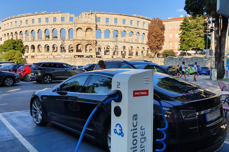 © Carsten Manns E-Auto steht an einer Ladesäule, ein Amphitheater im Hintergrund.