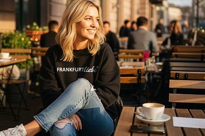 Frau sitzt mit einem Frankfurtliebe Pullover in einem Cafe