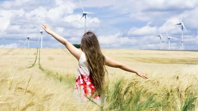 Mädchen läuft über Feld mit Windrädern im Hintergrund
