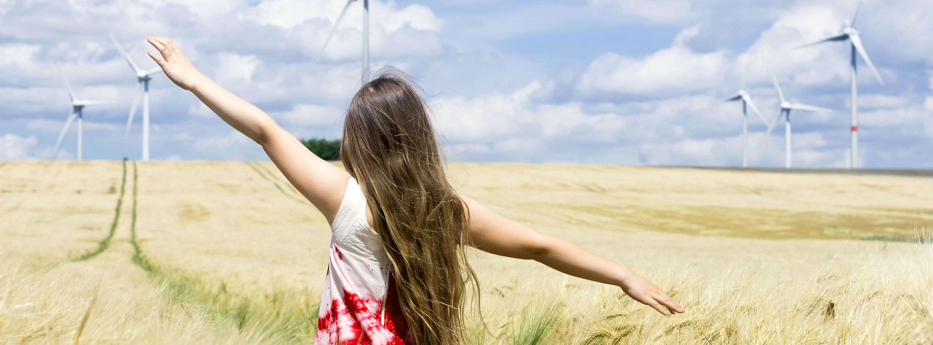 © iStock.com/kamisoka Mädchen läuft über Feld mit Windrädern im Hintergrund