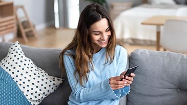 Frau sitzt mit Smartphone auf dem Sofa