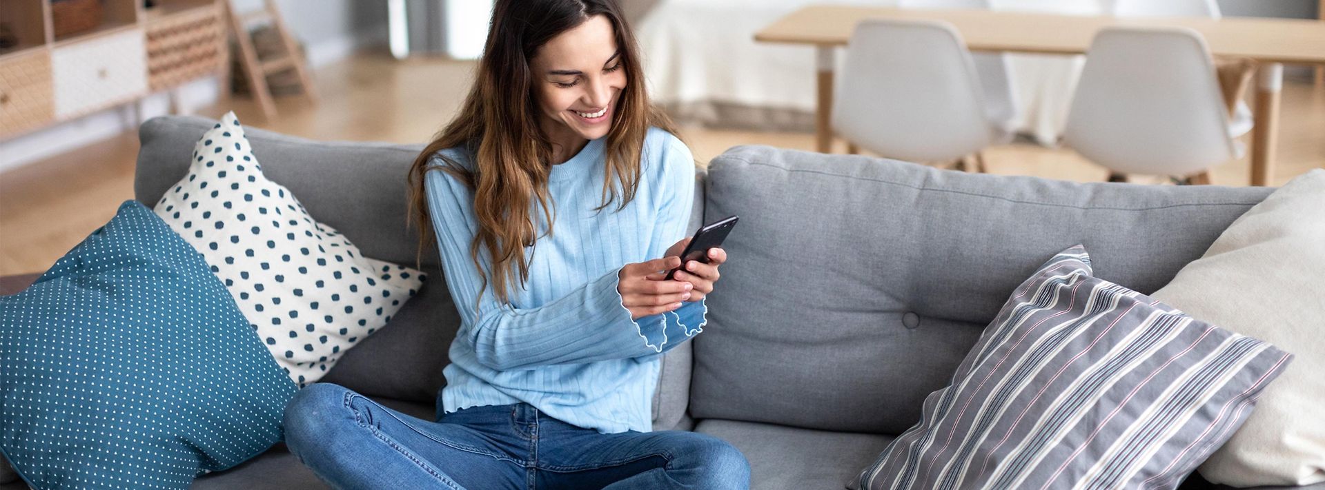© stock.adobe.com/BestForYou Frau sitzt mit Smartphone auf dem Sofa