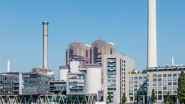 Ein modernes Industriegebäude mit mehreren Schornsteinen und großen Tanks vor einem klaren blauen Himmel.