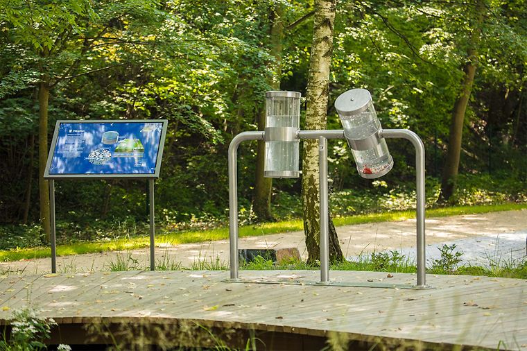 Zwei Wasserbehälter und ein Schild in einem Waldgebiet.