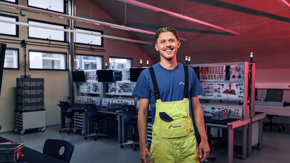 Auszubildender steht in einem Werkraum und lächelt zentral in die Kamera 