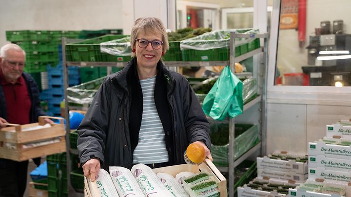 Dame mit kurzen grauen Haaren lächelt und trägt eine Vorratskiste