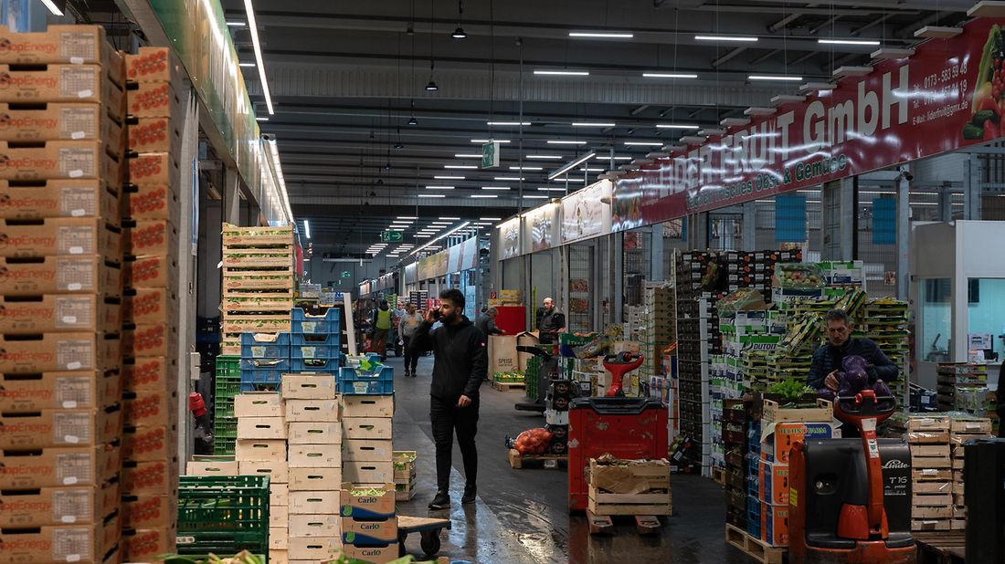 Ein Großmarkt mit gestapelten Kisten und Paletten, Menschen arbeiten und bewegen Waren.