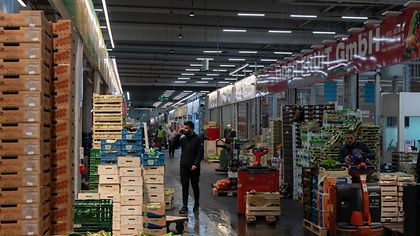 Ein Großmarkt mit gestapelten Kisten und Paletten, Menschen arbeiten und bewegen Waren.