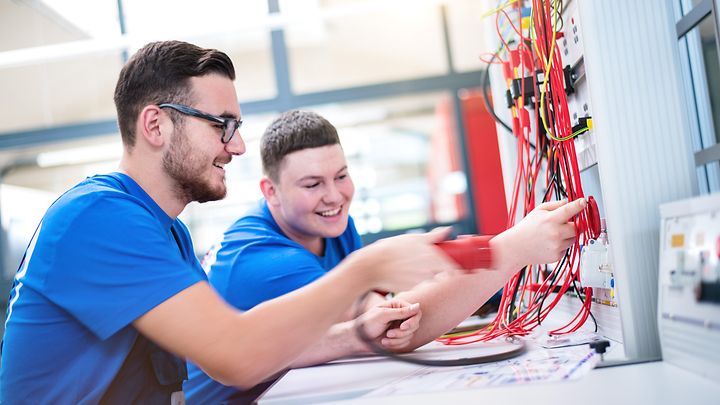 © Mainova/AndreFormer Zwei Auszubildende stecken Kabel in eine Schalttafel