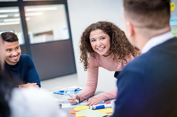 Auszubildende schreibt etwas auf Moderationskarten und lächelt.