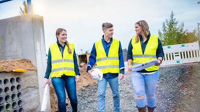 Gruppe Auszubildender läuft durch eine Baustelle und sprechen miteinander